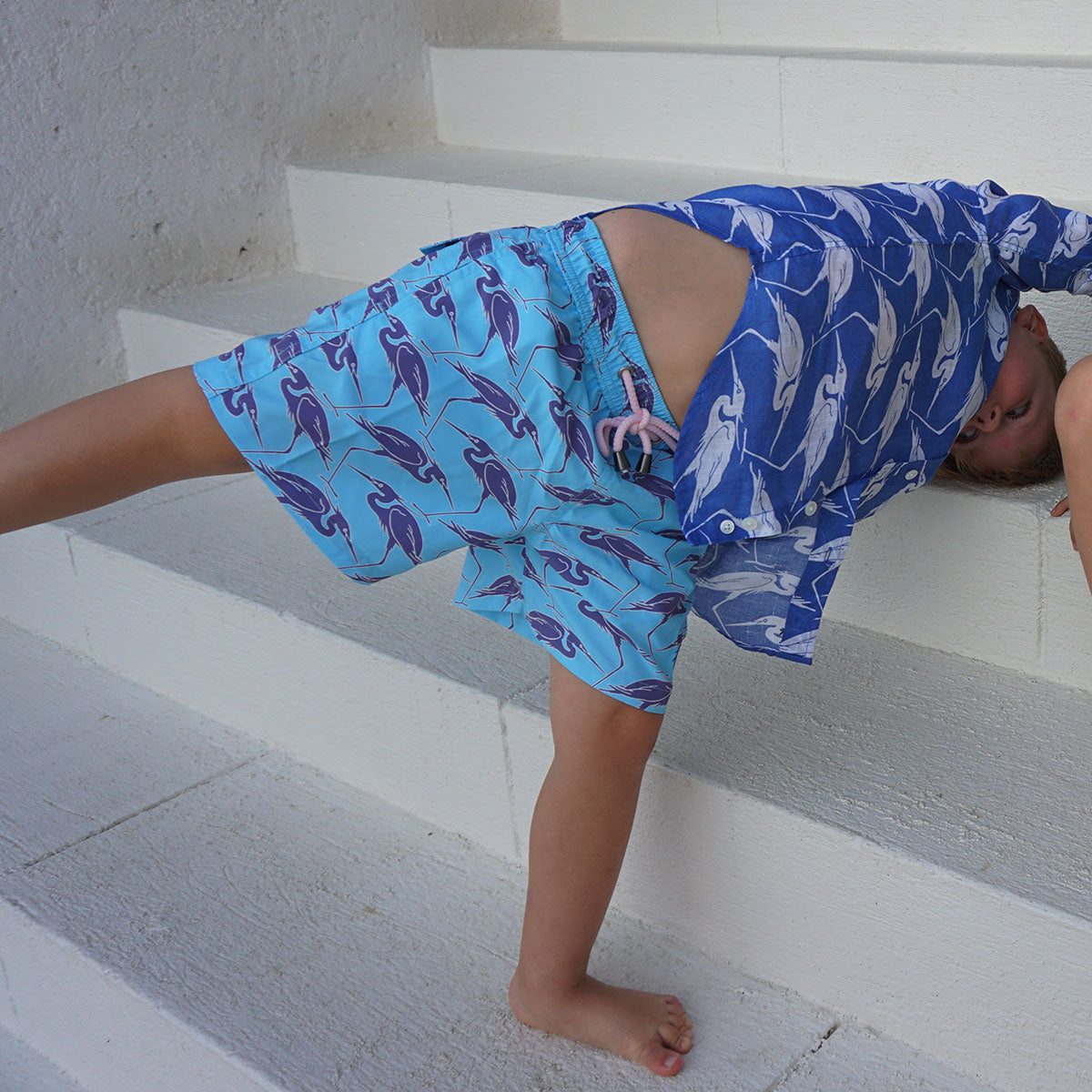 Boys cartwheel in sustainable turquoise blue swim shorts with Egret bird print