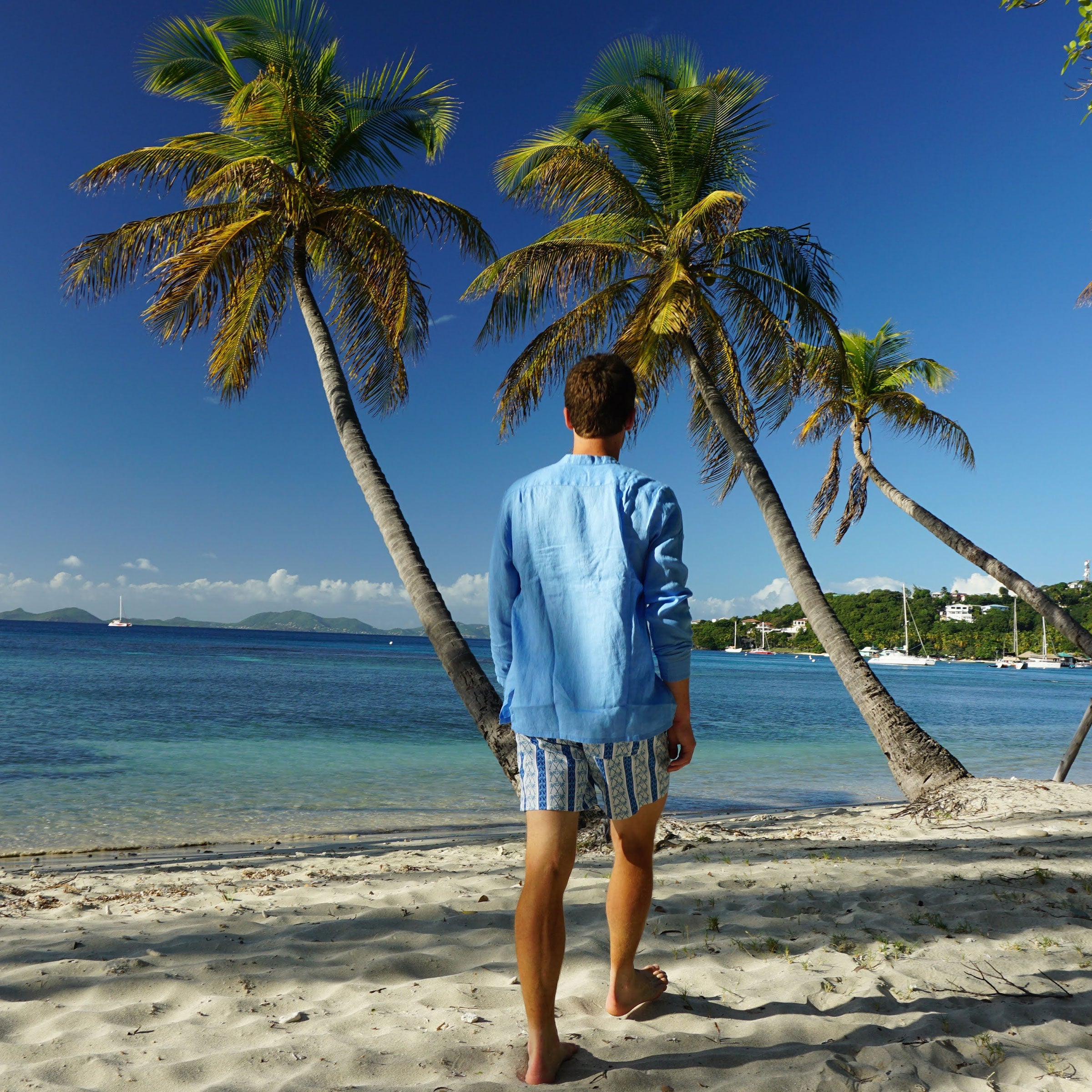 Mens swim shorts in NAVY PALM STRIPE walking on Britannia Bay Mustique 